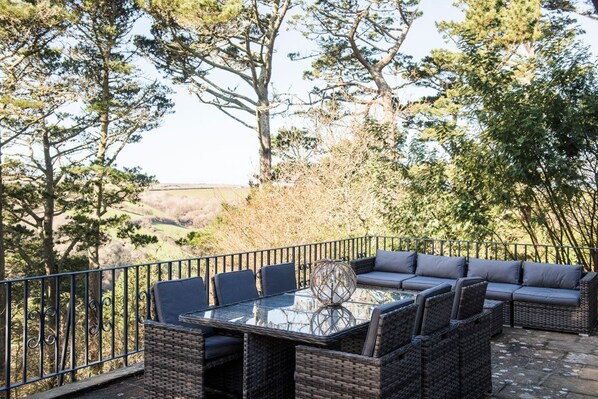 Un patio exterior con mobiliario de mimbre, una mesa de vidrio y vistas al campo.