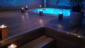 Un espace spa doté d’un sol en bois, d’une petite piscine et de plusieurs bougies.