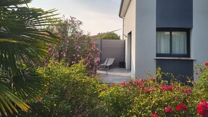 Une maison moderne avec un toit plat, un balcon et un jardin agrémenté de diverses plantes et fleurs.