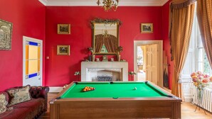 Une pièce avec une table de billard, une cheminée et un mur rouge.
