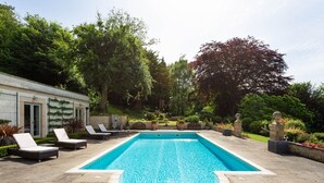 Une piscine rectangulaire avec une plage en pierre, entourée de chaises longues et d’un mur en pierre.