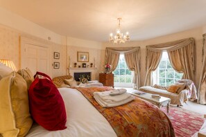 Une chambre spacieuse avec un grand lit, un coin salon, une cheminée et un lustre.