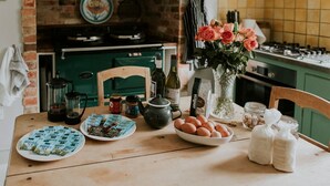 Una cocina con pared de ladrillo rústica, estufa verde y mesa de madera con bolsitas de té, huevos y un jarrón con flores.