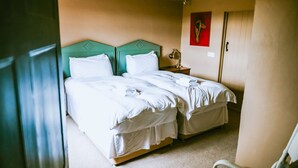Quarto com duas camas, cada uma com cabeceira verde, roupa de cama branca e uma pequena mesa de cabeceira com abajur.