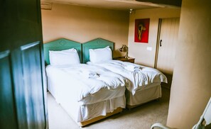 A room with two beds, each with a green headboard, white bedding, and a small bedside table with a lamp. - Stour Valley Cottage (Wimborne)