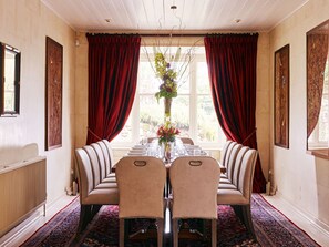 A formal dining room with a long table set for six, flanked by two sofas and red curtains. - Dartmoor Tea House - Seven Bedroom Villa, Sleeps 12 (Belstone)