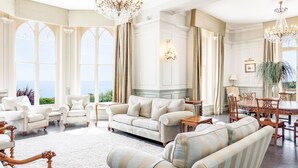 A spacious living room with a large window offering a view of the sea, elegant furniture, and a chandelier. - Dorset Castle - Nine Bedroom Castle, Sleeps 20 (Easton)