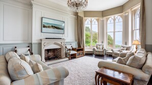 A spacious living room with a fireplace, comfortable seating, and large windows offering a view of the outdoors. - Dorset Castle - Nine Bedroom Castle, Sleeps 20 (Easton)