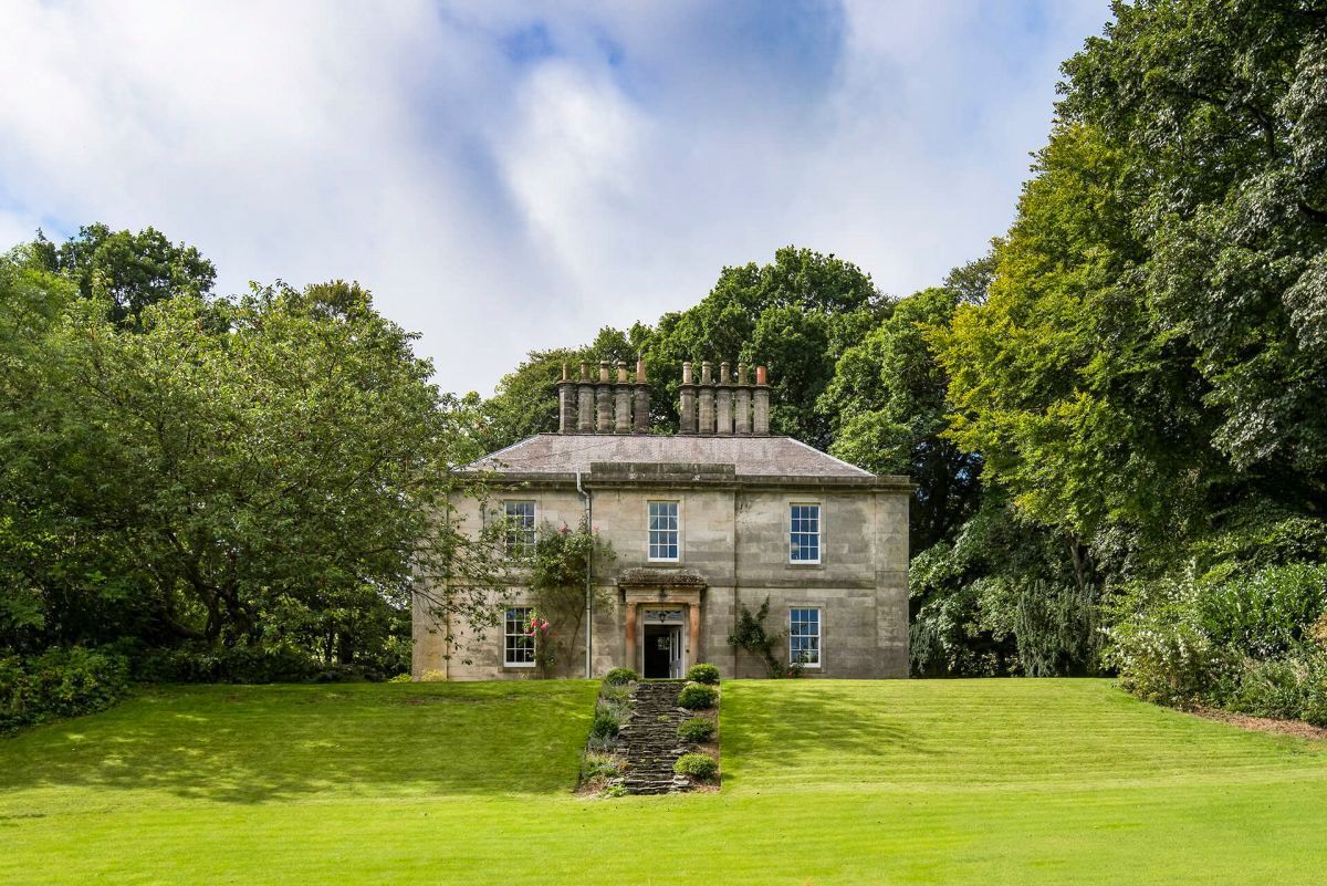A stone building with a symmetrical facade, a central entrance, and a well-maintained lawn.