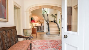 Un couloir agrémenté d’un tapis à motifs, d’un banc en bois, d’un vase décoratif et d’un escalier menant à un deuxième étage.