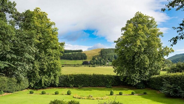 A well-maintained garden with a variety of trees and shrubs, a neatly trimmed lawn, and a clear view of the surrounding landscape.