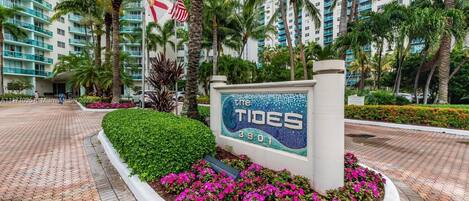 A hotel entrance with a sign reading "The Tides 3901", surrounded by palm trees and a paved walkway.