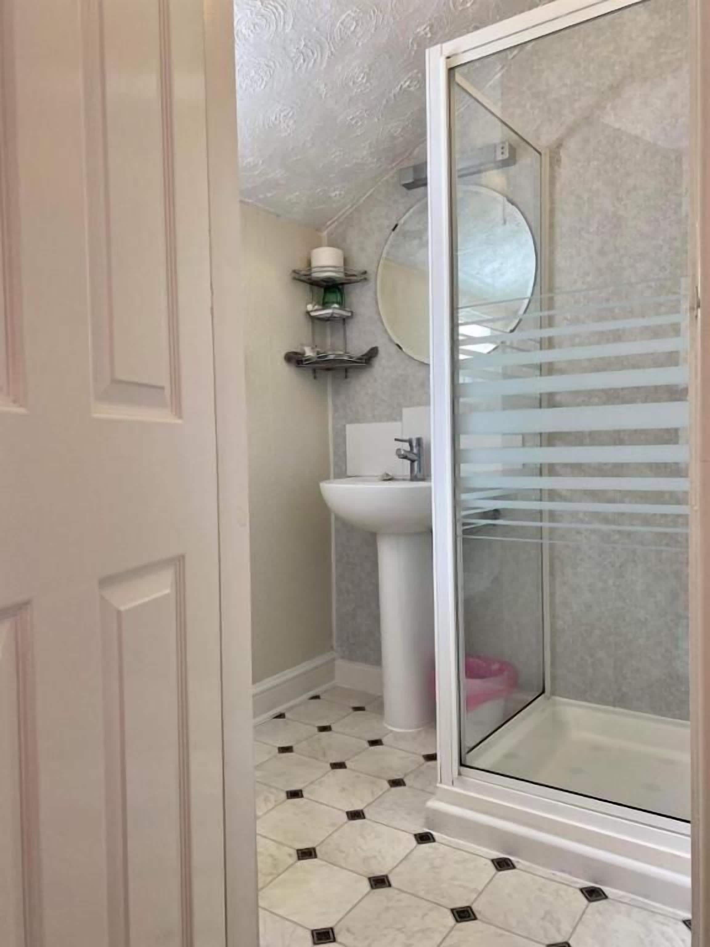 Une salle de bain avec une douche à parois de verre, un lavabo sur colonne et un miroir rond.