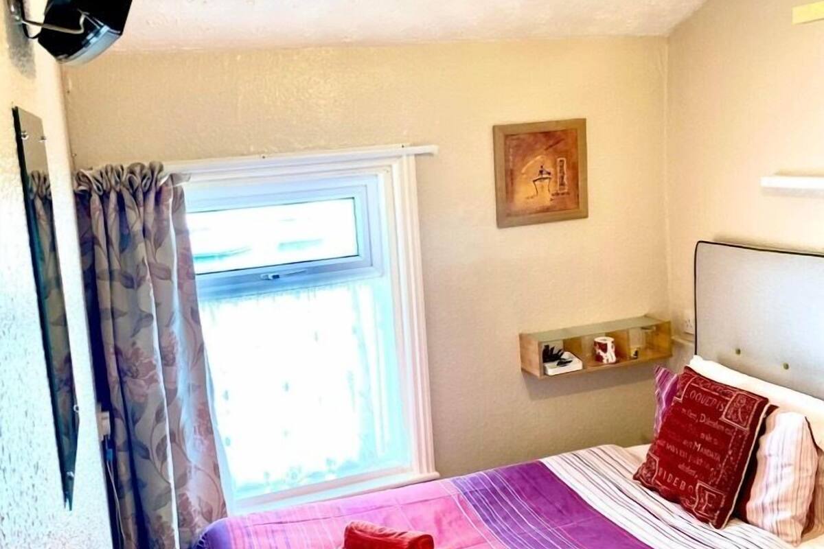 Un dormitorio con una cama, un ventanal, una lámpara de techo y un estante fijado a la pared.