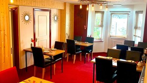 Ruokailutila, jossa on puupöytiä ja -tuoleja, kattokruunu ja punainen matto.
