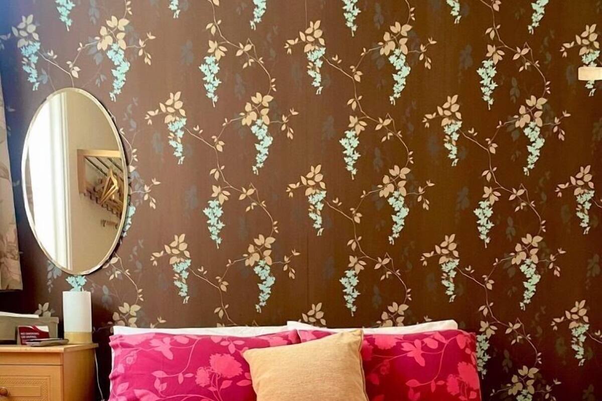 Una cama bien hecha con ropa de cama de estampado floral, una mesita de noche con una lámpara y una pared con diseño de papel tapiz floral.