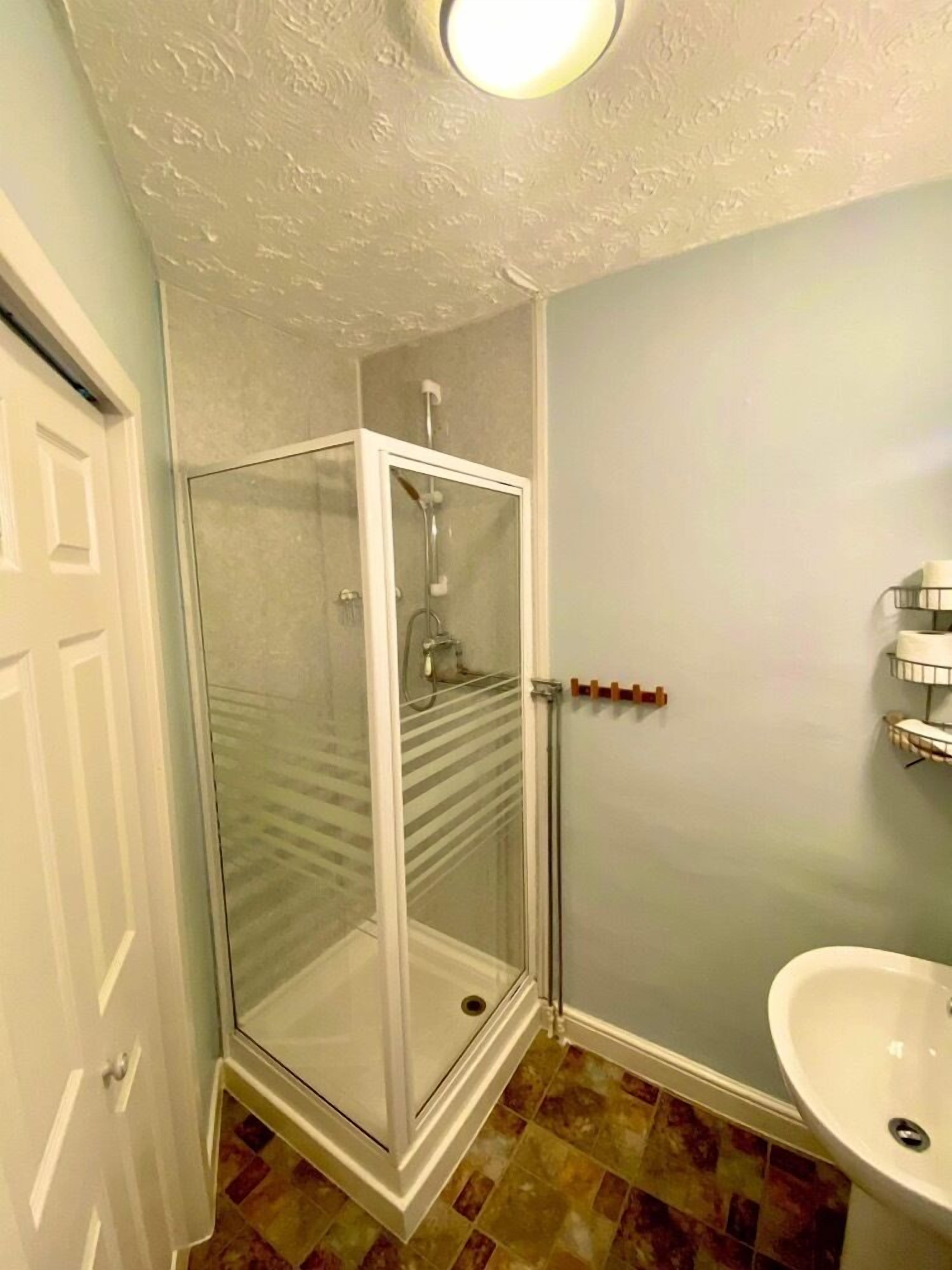 Un baño con ducha de vidrio, lavamanos y puerta.