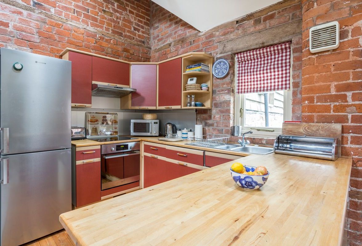 A compact kitchen with red cabinets, a stainless steel refrigerator, a microwave, and a wooden countertop.