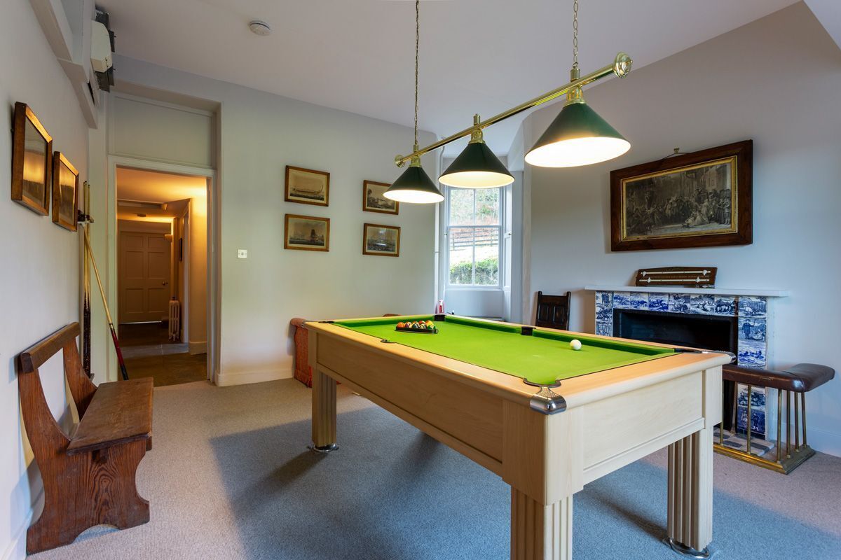 A pool table with two overhead lamps, a fireplace with a blue and white tiled surround, and a door leading to another room.