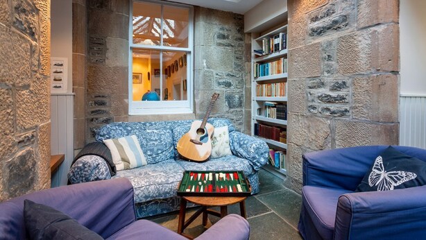 Une pièce chaleureuse avec un mur en pierre, un canapé bleu à motifs, une bibliothèque et une lucarne.