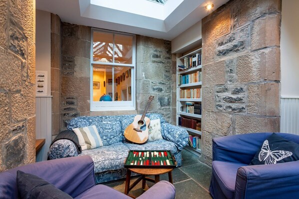 A cozy room with a stone wall, a blue patterned sofa, a bookshelf, and a skylight.