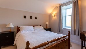 Une chambre à coucher avec un lit en bois, deux tables de chevet avec des lampes, une fenêtre avec des rideaux et un luminaire fixé au mur.