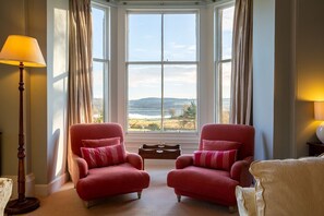 Une pièce avec deux fauteuils placés face à une grande baie vitrée donnant sur un paysage.
