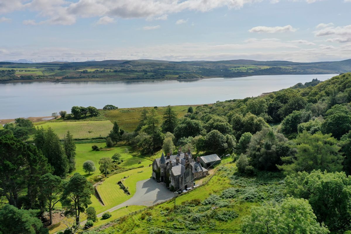 A large estate with a prominent building surrounded by lush greenery and a lake in the background.