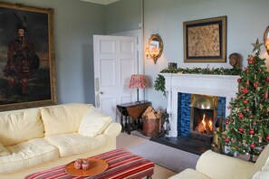 A cozy living room with a white fireplace, a Christmas tree, and a painting on the wall.