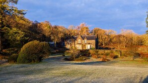 Une maison traditionnelle en pierre, dotée d’une façade symétrique, entourée d’un jardin bien entretenu et d’arbres majestueux.