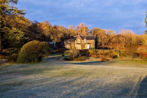 A traditional stone house with a symmetrical facade, surrounded by a well-maintained garden and mature trees.
