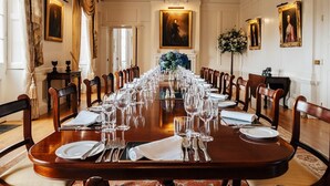 A formal dining room with a long table set for a meal, flanked by chairs, with a chandelier and framed portraits on the walls. - Tamar Castle - Eleven Bedroom Castle, Sleeps 22 (Landulph)
