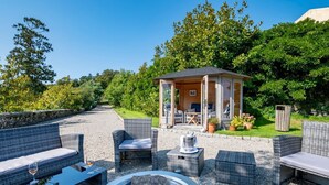 An outdoor seating area with wicker furniture, a fire pit, and a gazebo with a table and chairs. - Tamar Castle - Eleven Bedroom Castle, Sleeps 22 (Landulph)