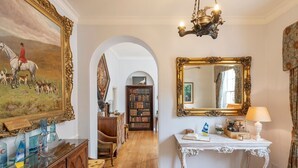 A room with a wooden floor, a white console table with a lamp, a large ornate mirror, and a painting of a horse and dogs. - Tamar Castle - Eleven Bedroom Castle, Sleeps 22 (Landulph)