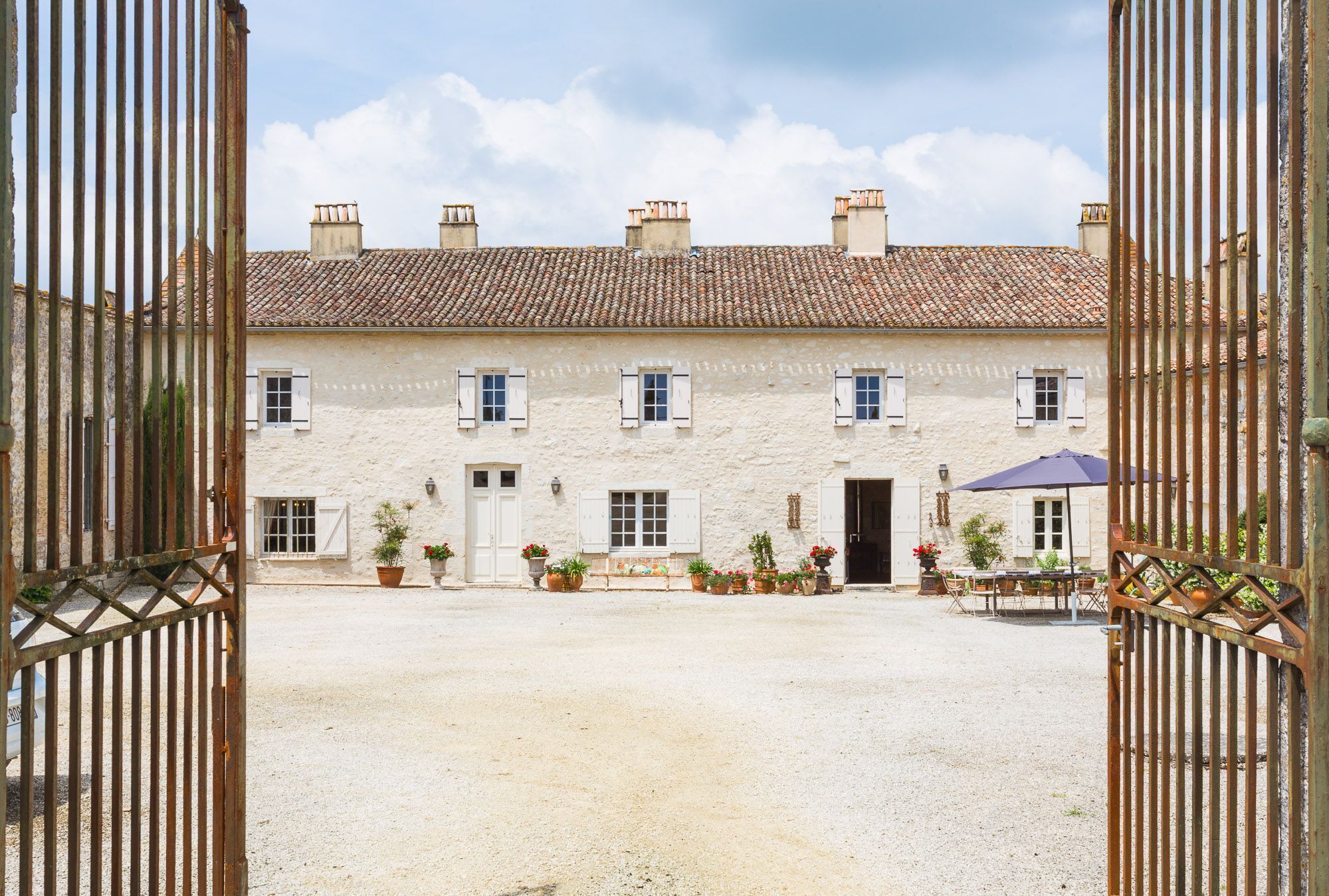 A two-story building with a tiled roof, a gravel courtyard, and a gated entrance.