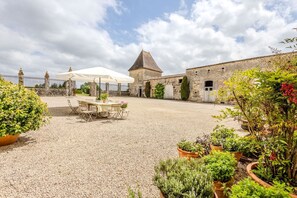 Une cour avec une table et des chaises sous une tonnelle, entourée de bâtiments en pierre et de plantes en pot.