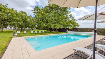 Une piscine entourée de verdure et d’un mur de pierre, avec des chaises longues et des parasols.