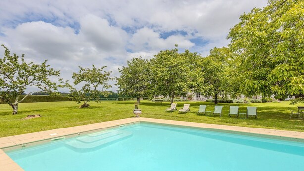 Une piscine avec des chaises longues et des arbres en arrière-plan.
