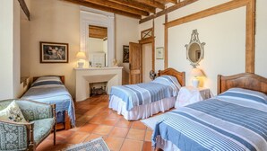 Une chambre avec deux lits, une cheminée, des poutres apparentes, un miroir et une chaise.
