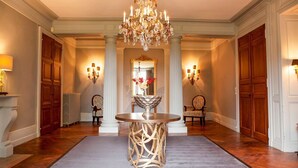 Un vaste hall d’entrée orné d’un lustre, une table ronde dotée d’un pied décoratif et deux chaises.