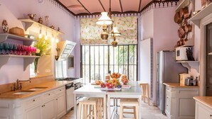 Une cuisine avec des meubles blancs, un îlot central doté de tabourets, une fenêtre avec des rideaux et un porte-ustensiles suspendu.