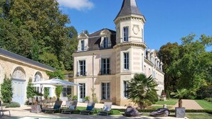 Un grand bâtiment historique doté d’une tour imposante et d’un espace piscine avec des chaises longues.