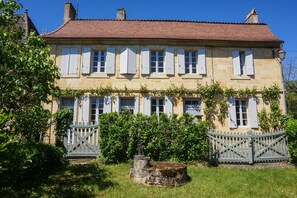A two-story stone building with white shutters, a red-tiled roof, and a gated entrance.
