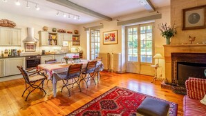 Uma sala de estar ampla com uma mesa de jantar, cadeiras, lareira e cozinha ao fundo.