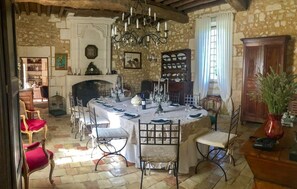A dining area with a round table set for four, surrounded by chairs. There is a fireplace with a mantel, a chandelier, and a bookshelf with various items. - Chateau De Neveu - Seven Bedroom Castle, Sleeps 14 (Saint-Martin-des-Combes)