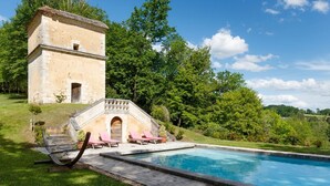 Una piscina con una estructura de piedra y sillones de descanso.