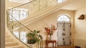 Una gran escalera con barandillas de metal ornamentadas, un candelabro y un cuadro en la pared.