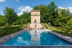 Una piscina con una estructura de torre al fondo, rodeada de exuberante vegetación.