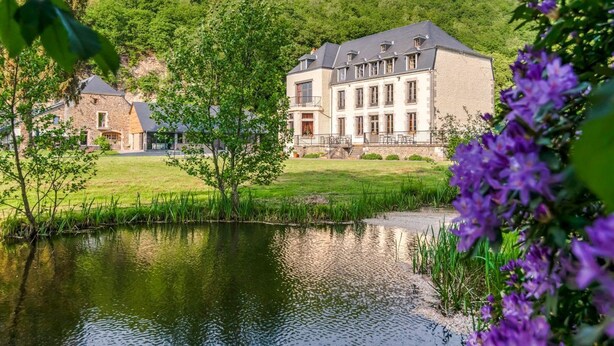 Un grand bâtiment situé devant un étang, entouré de verdure et de collines.