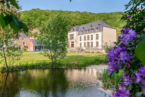 Un grand bâtiment situé devant un étang, entouré de verdure et de collines.